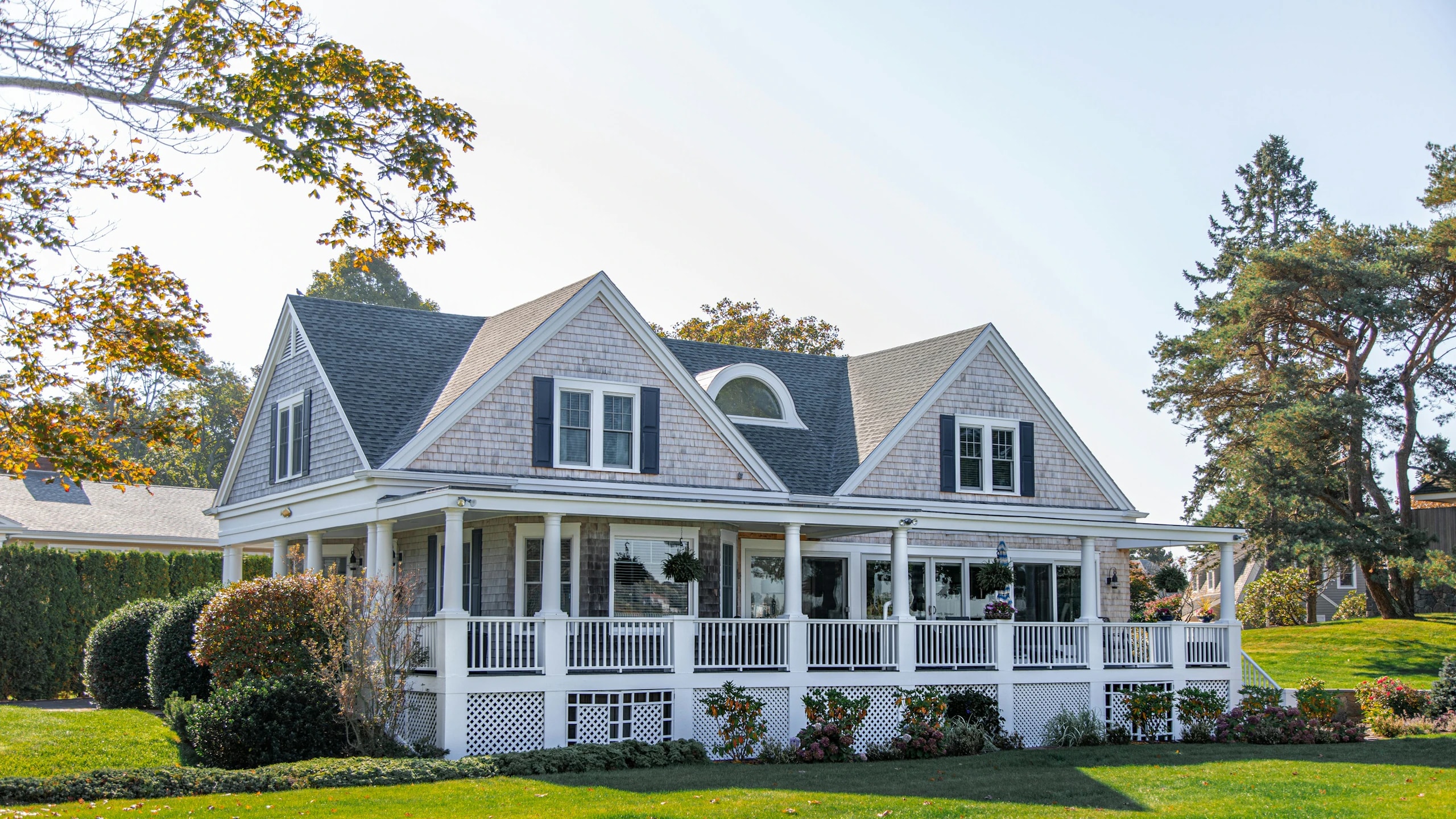 A white family house with a wraparound porch and a green lawn